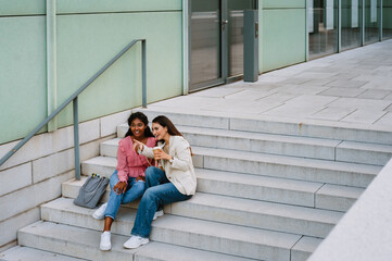 Young indian women smiling and drinking coffee while sitting on stairs