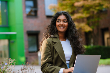 Joyful woman smiling and using laptop while sitting on city street