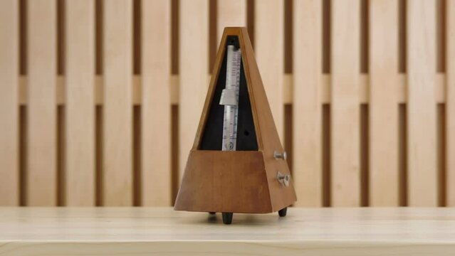 Mechanical metronome in wooden case on a wooden table in action. Filmed with studio light on a wooden background. Made with reverse.