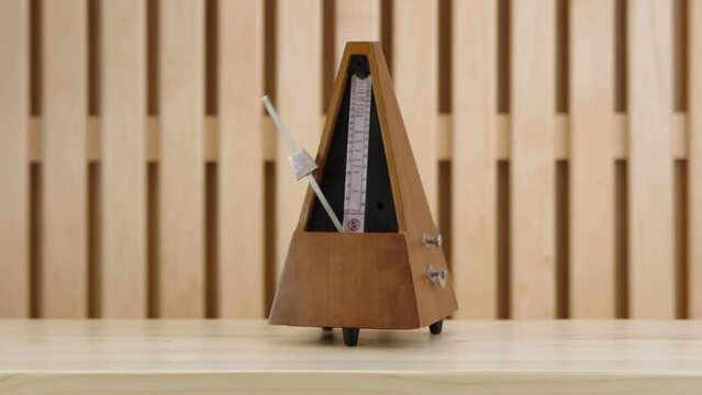 Mechanical metronome in wooden case on a wooden table in action. Filmed with studio light on a wooden background.