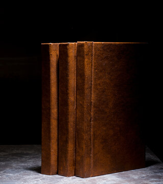 several books with the same binding on a dark background isolated. three books with a brown cover without inscriptions and titles with free space for text