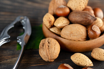 variety of nuts in a wooden bowl and nutcracker on wooden table, close-up.