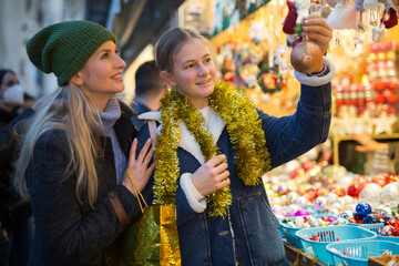 Happy mother with daughter choosing Christmas decoration and balls at Christmas market in evening