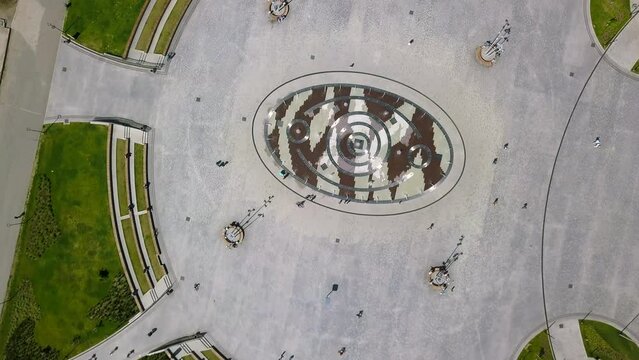 Top view of city square with fountain in summer. Clip. Modern design of fountain in center of square in busy city. Modern square with people and fountain on summer day