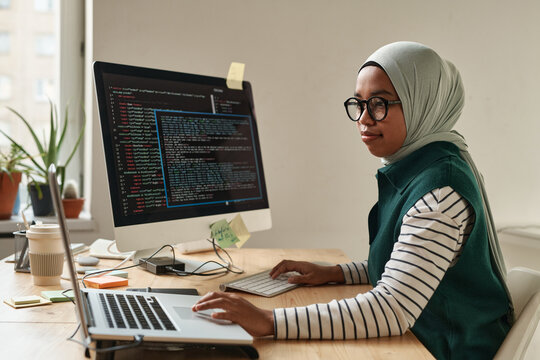 Side view of young intern or professional software developer touching laptop touchpad while looking through online information