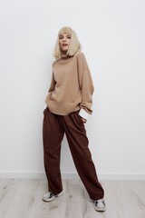 a beautiful woman stands full-length on a light background in a sweater and shirt, put her hands in her pants pocket looking down slightly covering her face with her hair