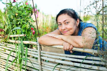 Happy smiling elderly woman amateur gardener standing leaning on wooden fence of vegetable garden...