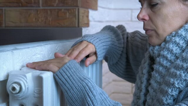 Woman in unheated apartment. A sad woman in knitted woolen clothes get warm in unheated room because of expensive heating costs.