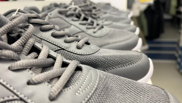 Gray fabric running shoes are lined up on the shelf of a sports shoe store. Closeup shot