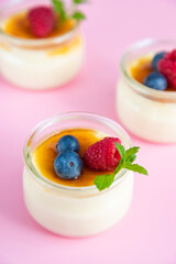French custard dessert creme brulee with crispy caramel crust and fresh berries on a pink background.