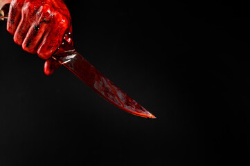 A man with bloody hands brandishes a knife on a black background.  © Михаил Решетников