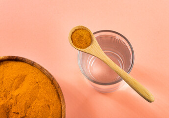 Spoon with organic turmeric and glass of filtered water - Curcuma longa