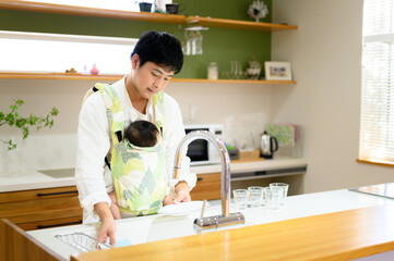 赤ちゃんを抱っこしながらワンオペ家事をするパパさん　右にコピースぺースあり © kapinon