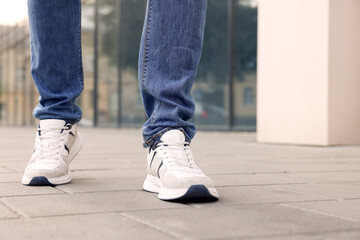 Fototapeta na wymiar Man in jeans and sneakers walking on city street, closeup. Space for text