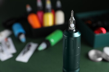 Naklejka premium Tattoo machine and tools on dark green table, closeup