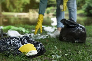 Woman collecting garbage in park, focus on paper cup. Space for text