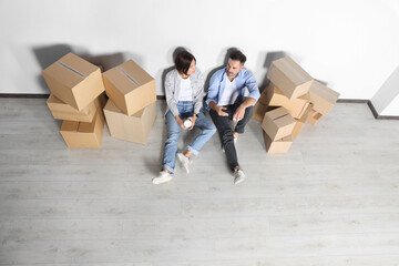 Happy couple with takeaway coffee resting on floor in new apartment, above view. Moving day