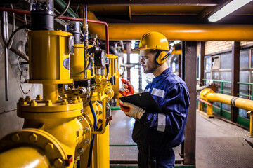 Heating plant worker taking notes about gas consumption and temperature inside energy power plant.