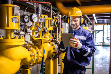Fototapeta premium Heating plant technician standing by gas pipes and maintaining temperature inside power plant boiler room.
