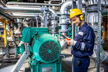 Blue collar worker standing by gas fuel engines inside power plant and analyzing results.