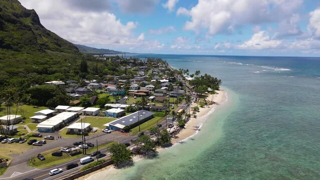 Drone aerial view of Kaaawa town and the coastline of the Pacific Ocean. Cars driving on Kamehameha Highway