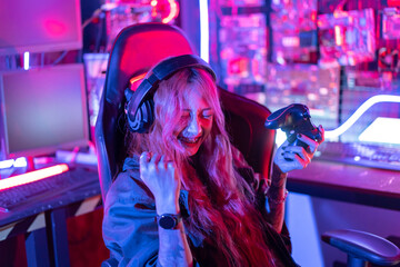 Fototapeta na wymiar You win. Gamer using joystick controller plays online video game with computer neon lights backgrounds, woman use gaming headphones playing live stream esports games console at home.