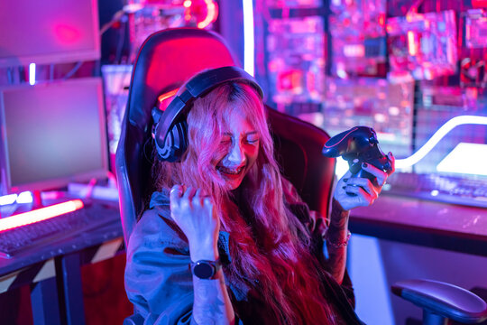 You win. Gamer using joystick controller plays online video game with computer neon lights backgrounds, woman use gaming headphones playing live stream esports games console at home.