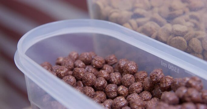 Dog paw picks up dry balanced food from plastic container with a metal spoon. Hand with scoop measures out portion of food for pet. Dog food allowances serving size. Puppy care nutrition rules. 