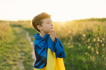 Ukrainian boy closed her eyes and praying to stop the war in Ukraine in a field at sunset. Hands...