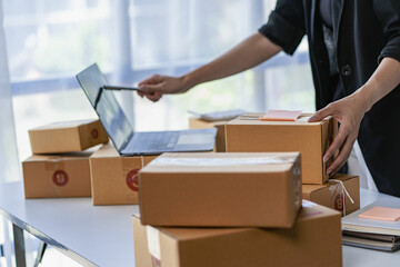 Online business idea, young sme entrepreneur, working from home with laptop and smartphone to take orders and deliver parcels.