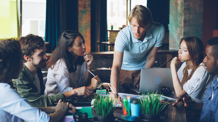 Multiracial group of professionals creative team is discussing charts and graphs developing working strategy at desk in shared office. Discussion, teamwork and workplace concept.