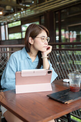 Happy Asian woman using computer tablet at coffee cafe