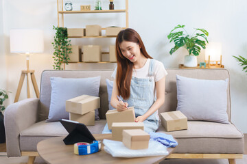 Obraz na płótnie Canvas Online merchant concept, Female entrepreneur look data on tablet and write address on parcel boxes