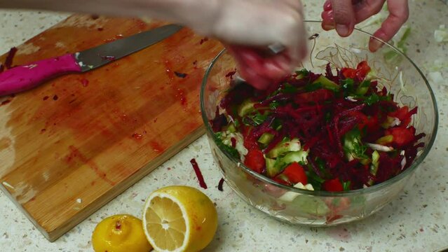 Kitchen table in home kitchen with vegetable salad being prepared. Close-up of female hands stirring fresh salad in a bowl with a tablespoon. Raw food is good for health