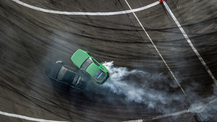 Aerial top view car drifting, Race drift car with lots of smoke from burning tires on speed track, Two car drifting battle on asphalt race track, Two drift cars battle with smoke from burned tire. © Darunrat