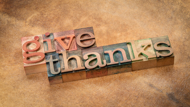 Give thanks word abstract in vintage letterpress wood type on a backlit background, Thanksgiving and fall holidays theme.
