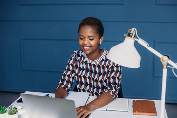 Shot of pretty happy young african-american entrepreneur woman sitting on her workplace in the...