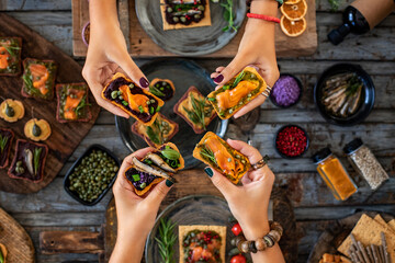 Sea food tapas and ricotta toast with capers at the hands of two women.