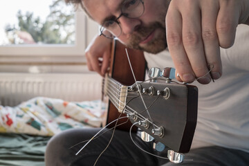 Acoustic guitar tuning. Focused man repairs a stringed musical instrument, indoors. 