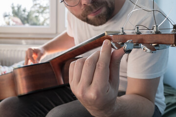 Acoustic guitar tuning. Focused man repairs a stringed musical instrument, indoors. 