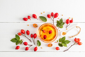 a glass bowl with organic natural rosehip seed oil among the fruits and leaves on a white wooden table. top view. antioxidant. a natural remedy.