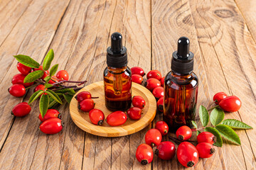 two cosmetic bottles with a pipette with an organic product based on rosehip seed oil on a wooden background among ripe rosehip berries. front view.