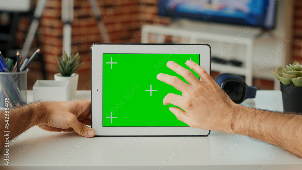Poster male freelancer looking at horizontal greenscreen on display, working with wireless tablet at desk. 