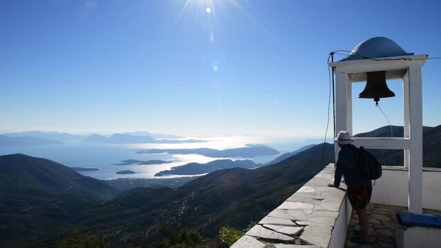 A tourist by a bell tower enjoying the mountain top view of the sea and islands below