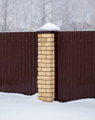 Brick pillar on the fence in the snow.