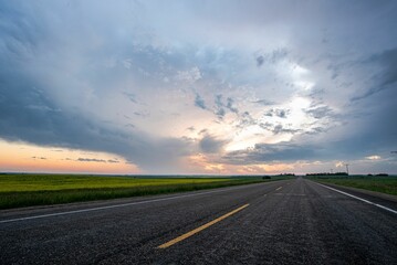 Beautiful display of a stormy sky captured along an asphalt road with yellow marking lines at sunset