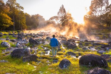 Male tourist standing and looking at Natural hot spring with steam, and rock in the morning at Chae Son National Park, Lampang, Thailand. - obrazy, fototapety, plakaty