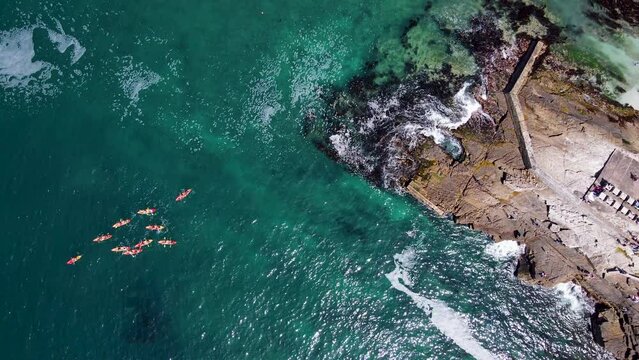 Top Down View Of Bright Kayaks Paddling Away From Rocky Coastline