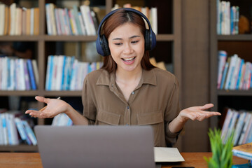 Asian tutor of language start online lesson with trainee wave hand smiling looks at pc screen. woman in headphones communicating distantly, e-learning process, application usage concept