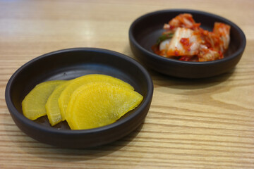 Pickled radish and kimchi are served as side dishes on a round plate.